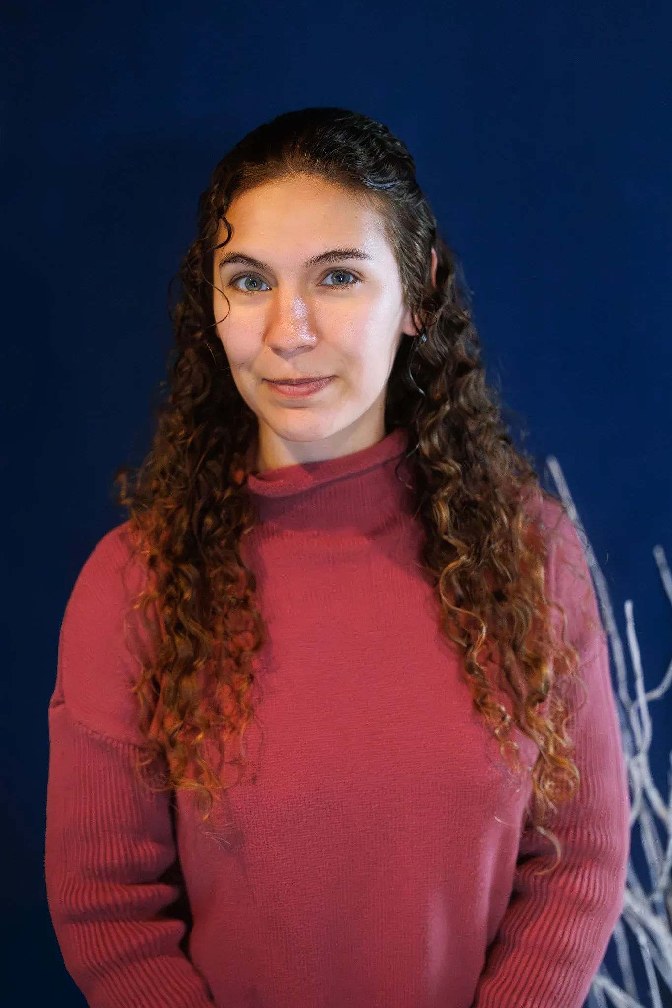 Headshot in a burgundy sweater against a blue background