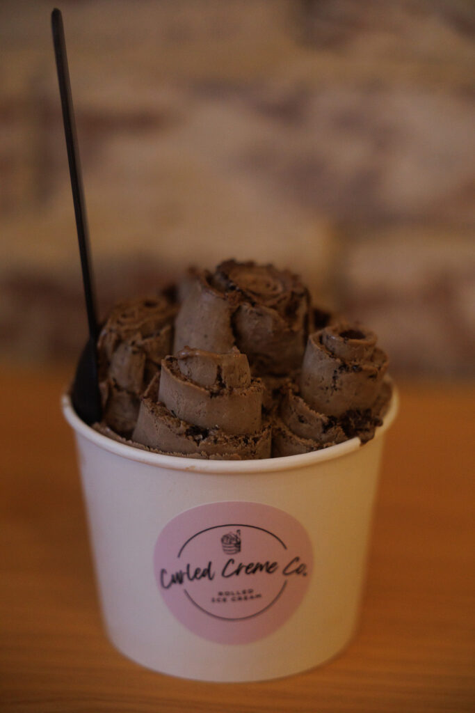 Rolled chocolate ice cream in a cup labeled “Curled Creme Co.” with a black spoon, served at Curled Creme Co. in DeRidder, Louisiana.