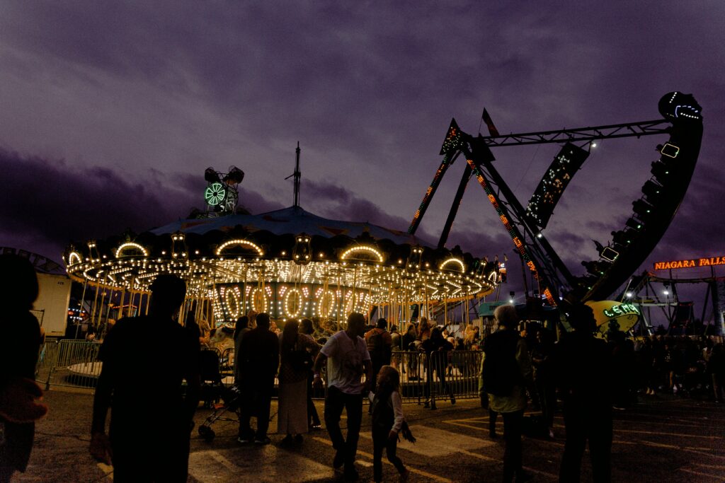 Evening at the Cal Cam Fair in Sulphur, LA—families and children enjoying a brightly lit carousel and carnival rides under a dramatic purple sky.